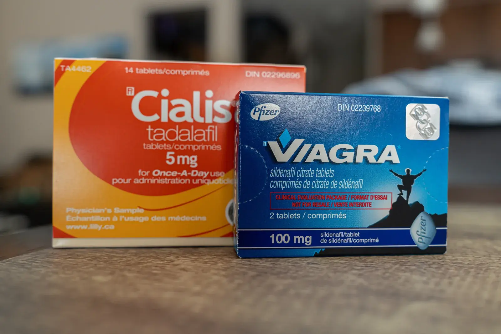 Boxes of Cialis 5mg and Viagra 100mg side by side on a wooden table